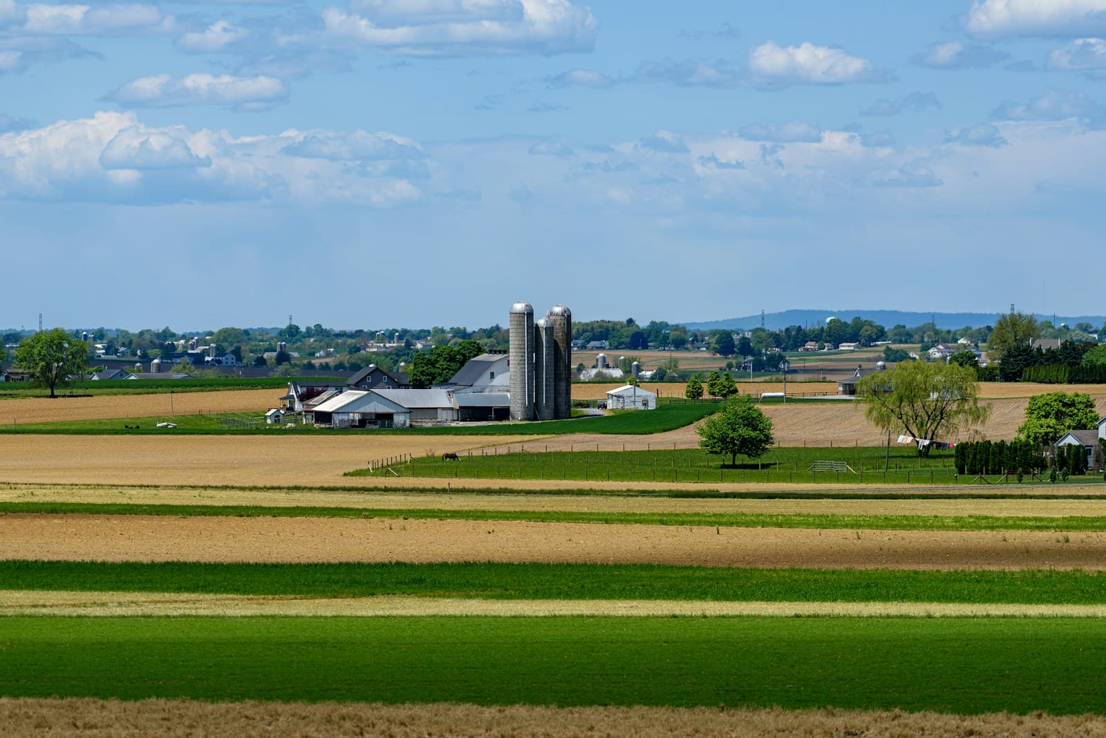 A ploughed field in the foreground with farm buildings and a grain silo in the distance